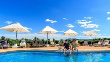 Una piscina al aire libre, sombrillas, sillones reclinables de piscina