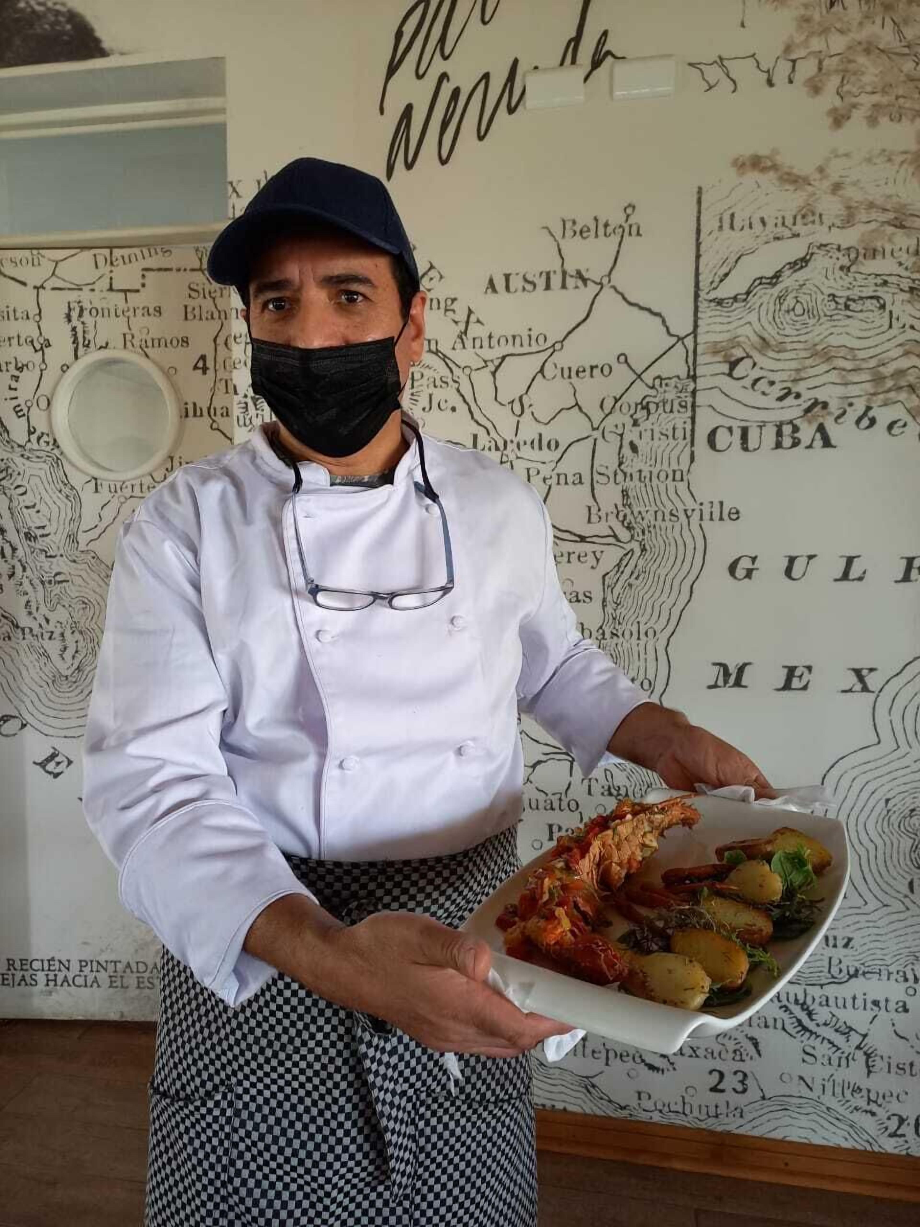 A chef holding a plate of food in front of a wall with a map.