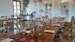 Una larga mesa de comedor dispuesta con sillas, un mural con texto y un retrato, y una araña.