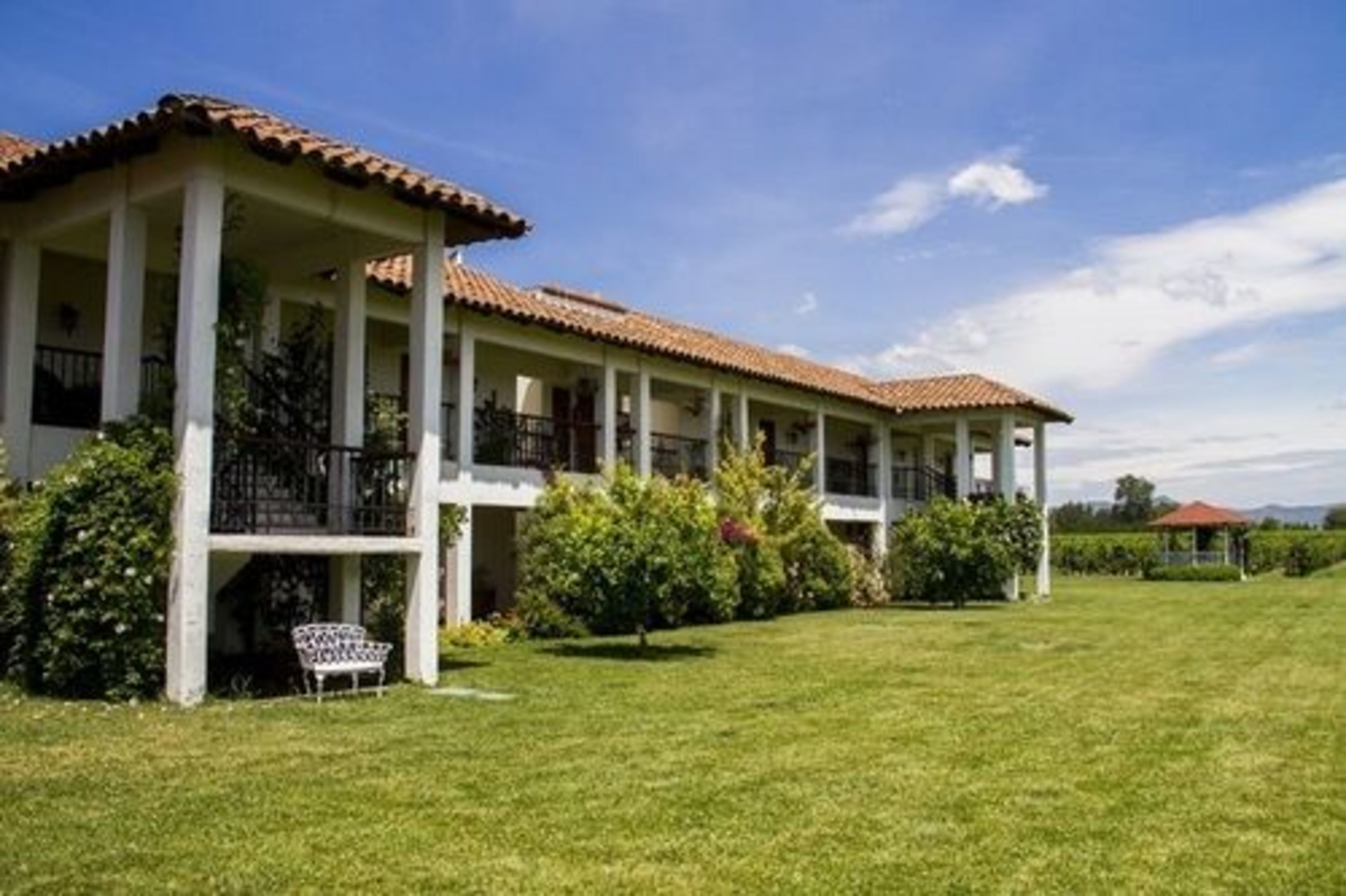 A two-story building with a tiled roof and white columns, surrounded by a well-maintained lawn and greenery.