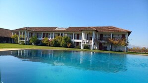 Una piscina grande con un edificio al fondo que tiene techo de azulejos y columnas.
