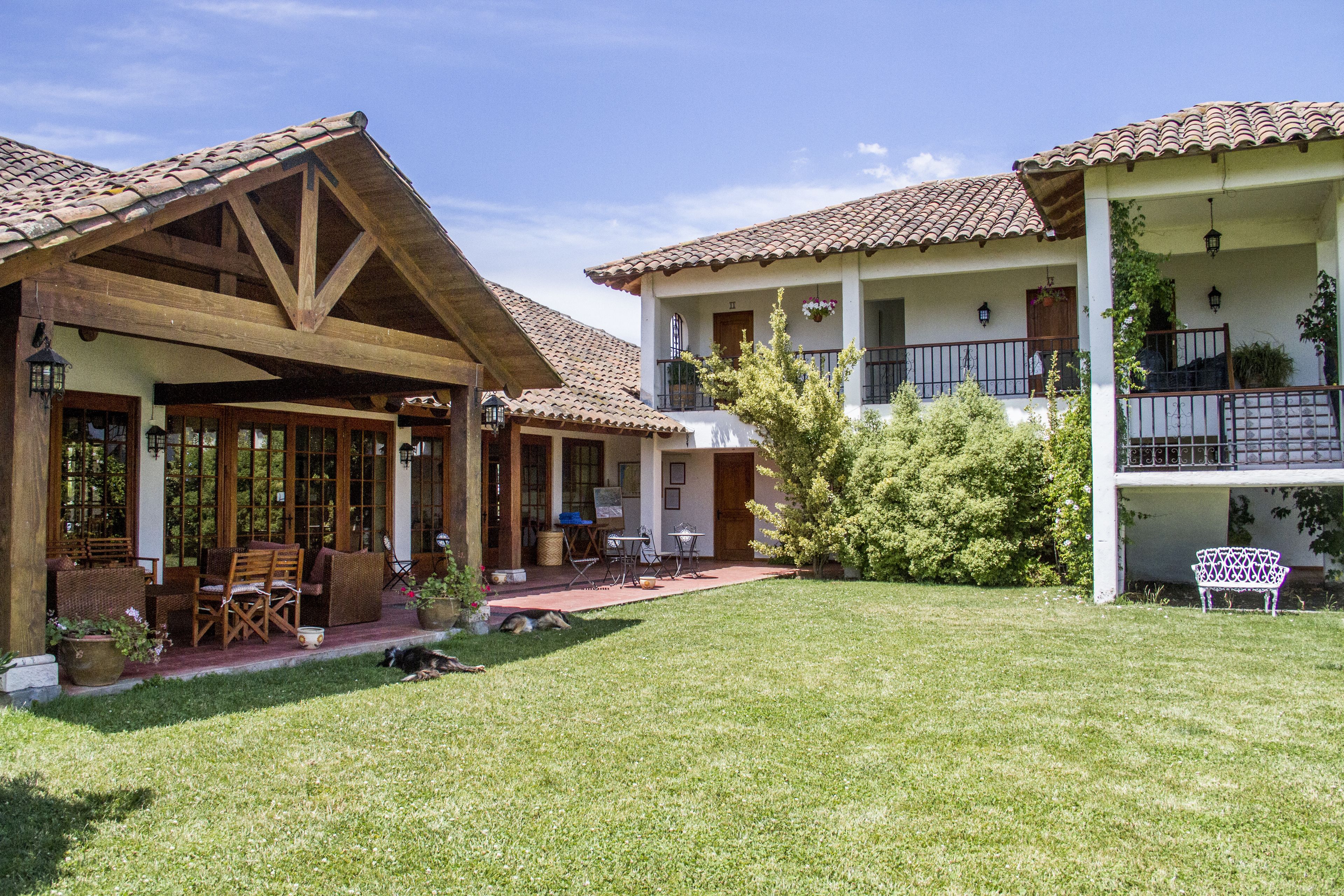 A two-story building with a tiled roof, a covered patio area with outdoor furniture, and a well-maintained lawn.