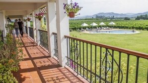 Un balcón cubierto con vistas a una piscina y viñedos.