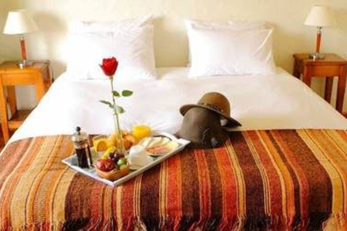 A neatly made bed with a striped bedspread, a tray of breakfast, a rose, and a hat on the bed.