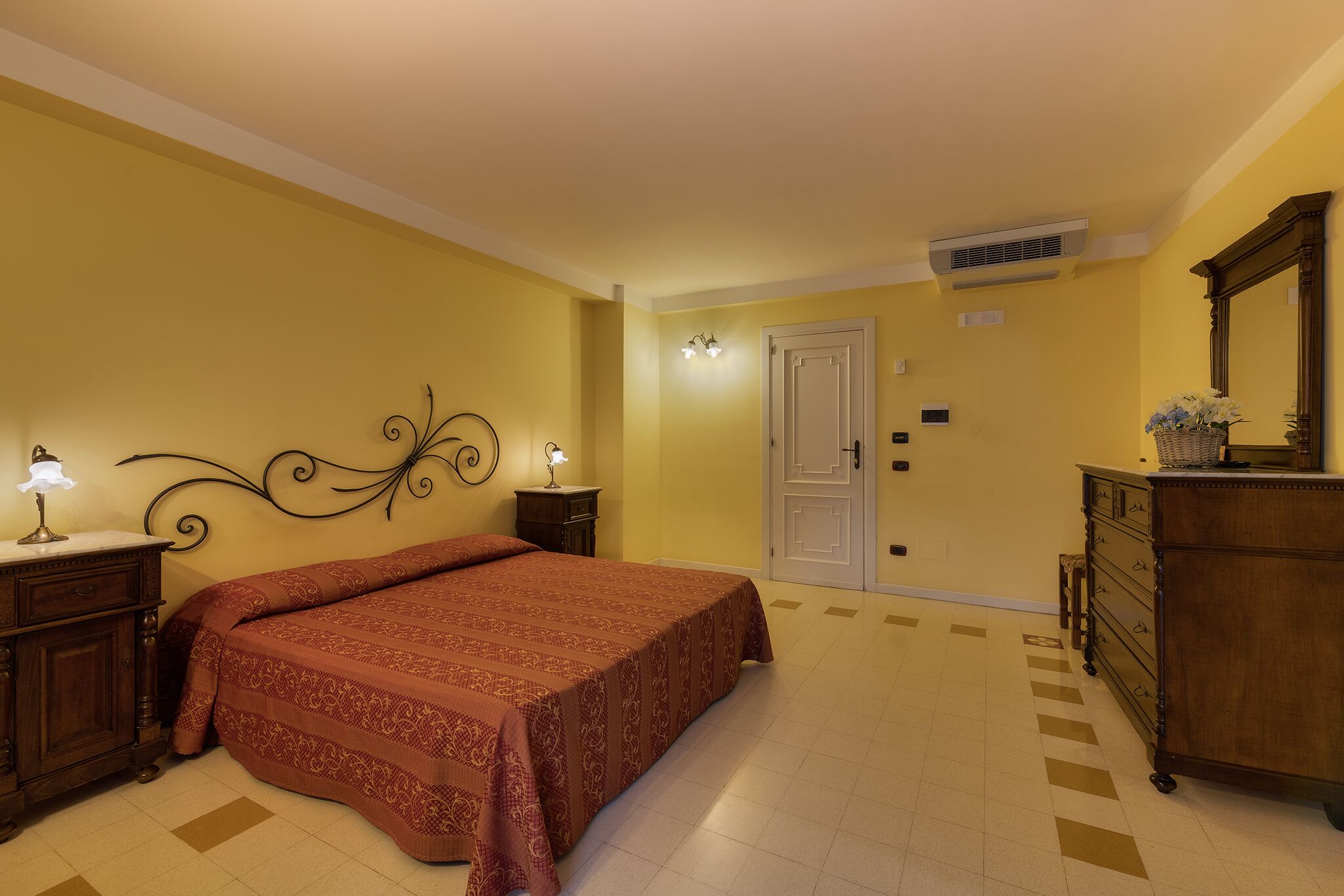 A bedroom with a large bed, a dresser, a nightstand, and a wall-mounted mirror.