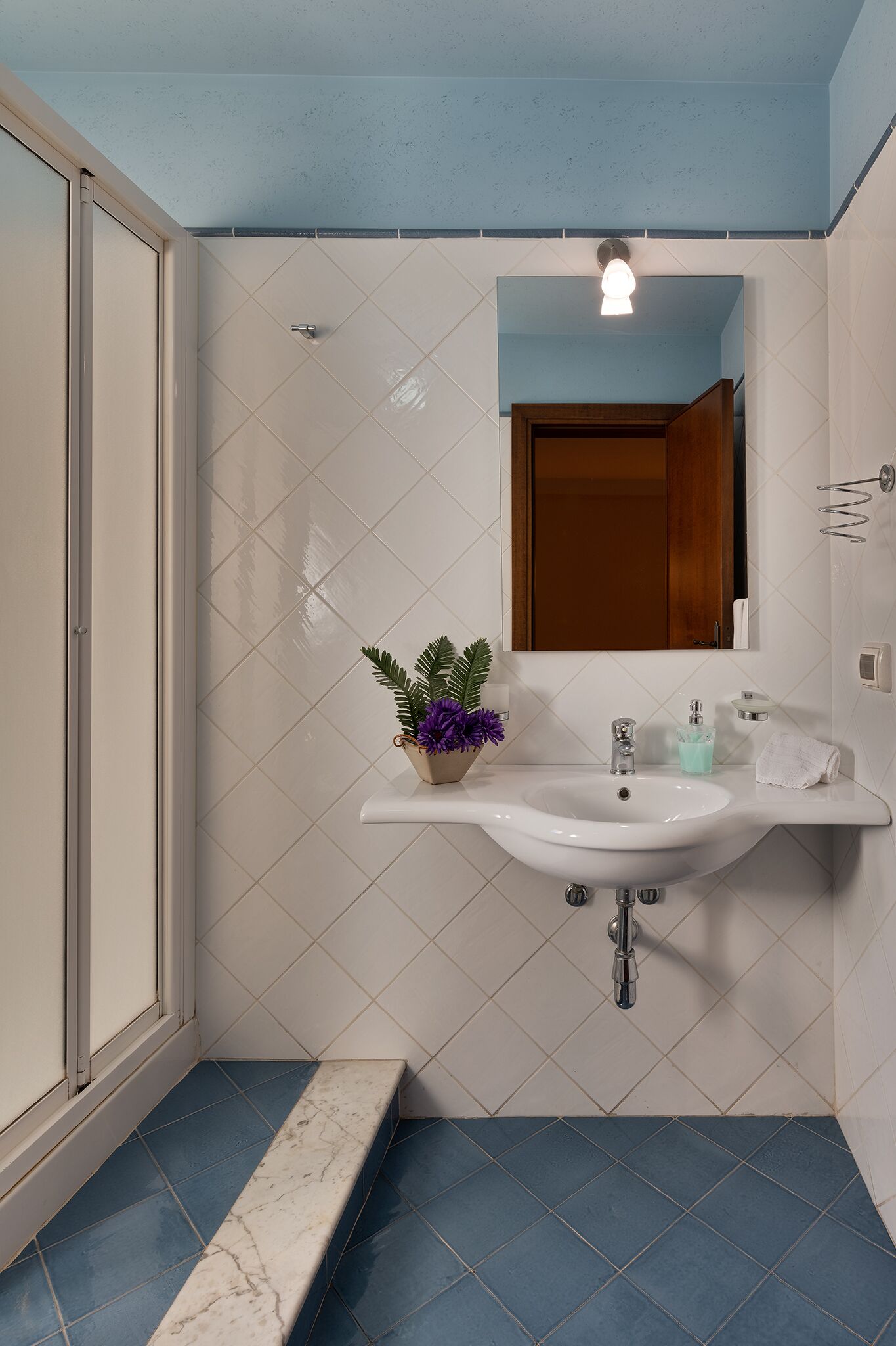 A bathroom with a white sink, a mirror, and a potted plant.