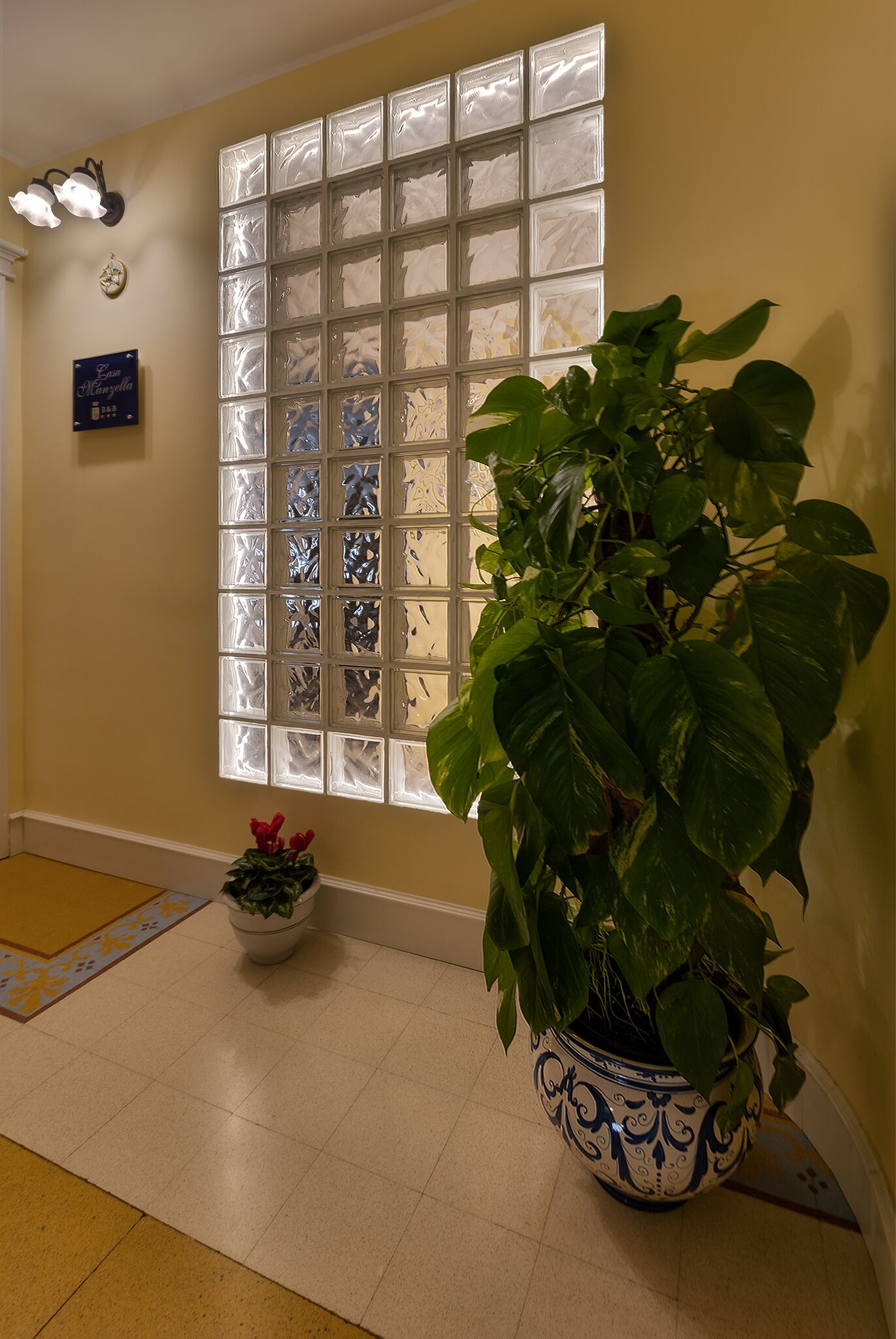 A hallway with a large window, a potted plant, and a decorative light fixture.
