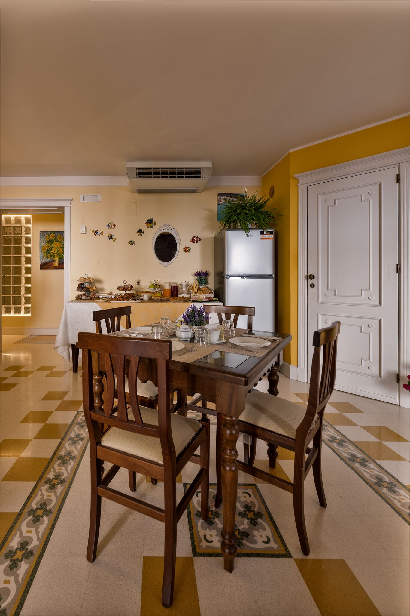 Un comedor con piso a cuadros, sillas de madera, una mesa de vidrio y una puerta blanca.
