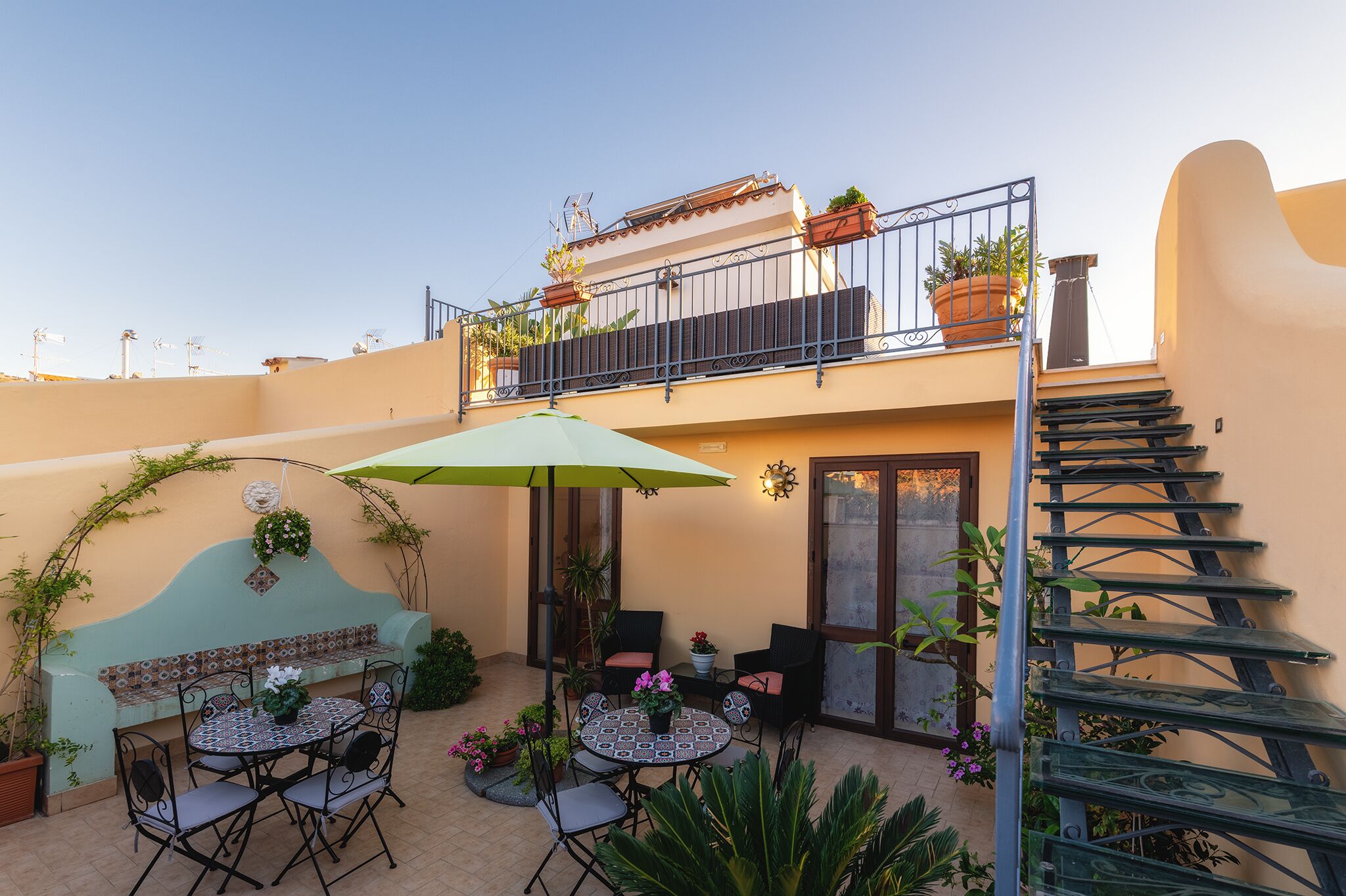 Un patio con una mesa redonda y sillas, un banco, plantas en macetas y una escalera.