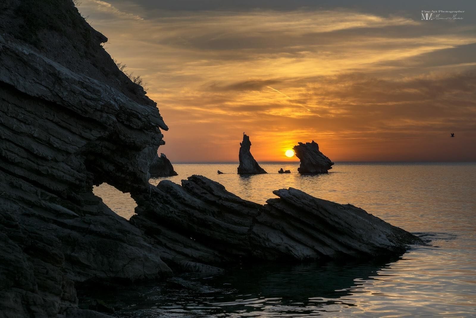 A coastal scene with rocky formations and a sunset over the water.