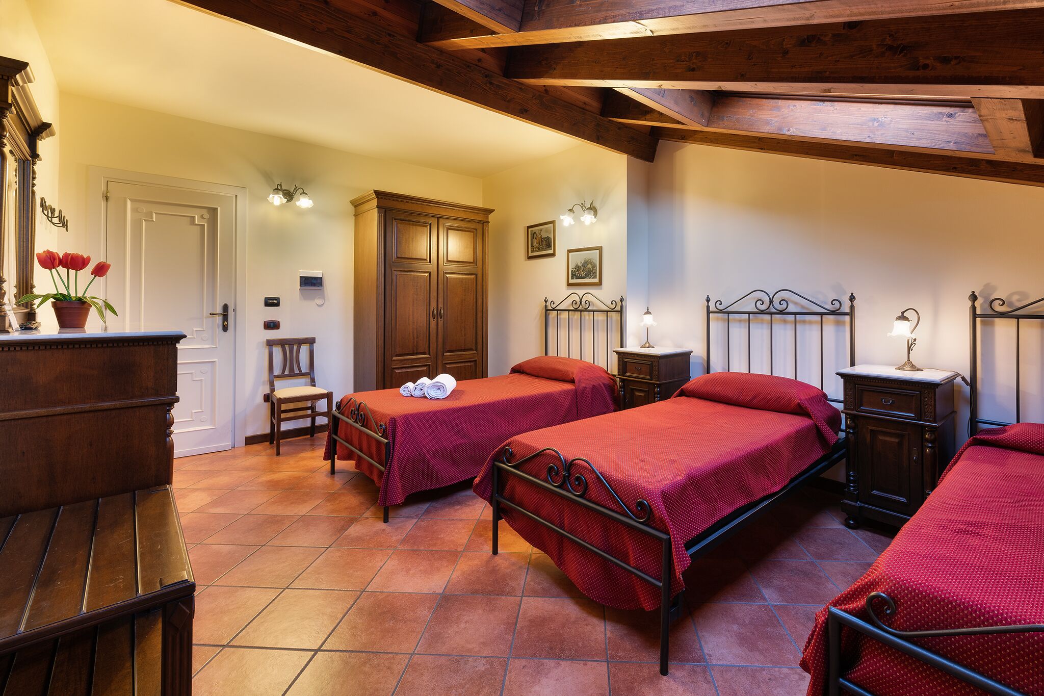 A room with two beds, a wooden wardrobe, a chair, and a small table with a potted plant.