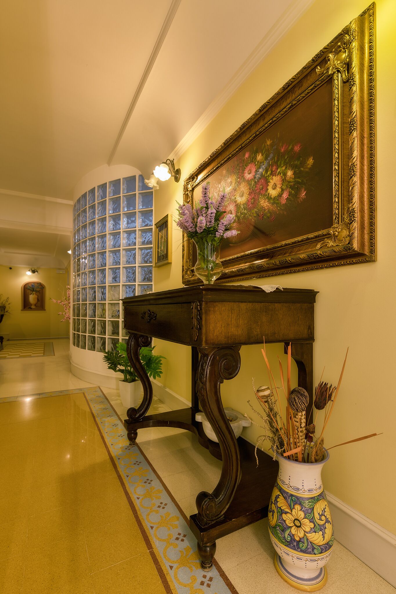 Un couloir orné d’un grand tableau, d’un vase de fleurs et d’un miroir décoratif.