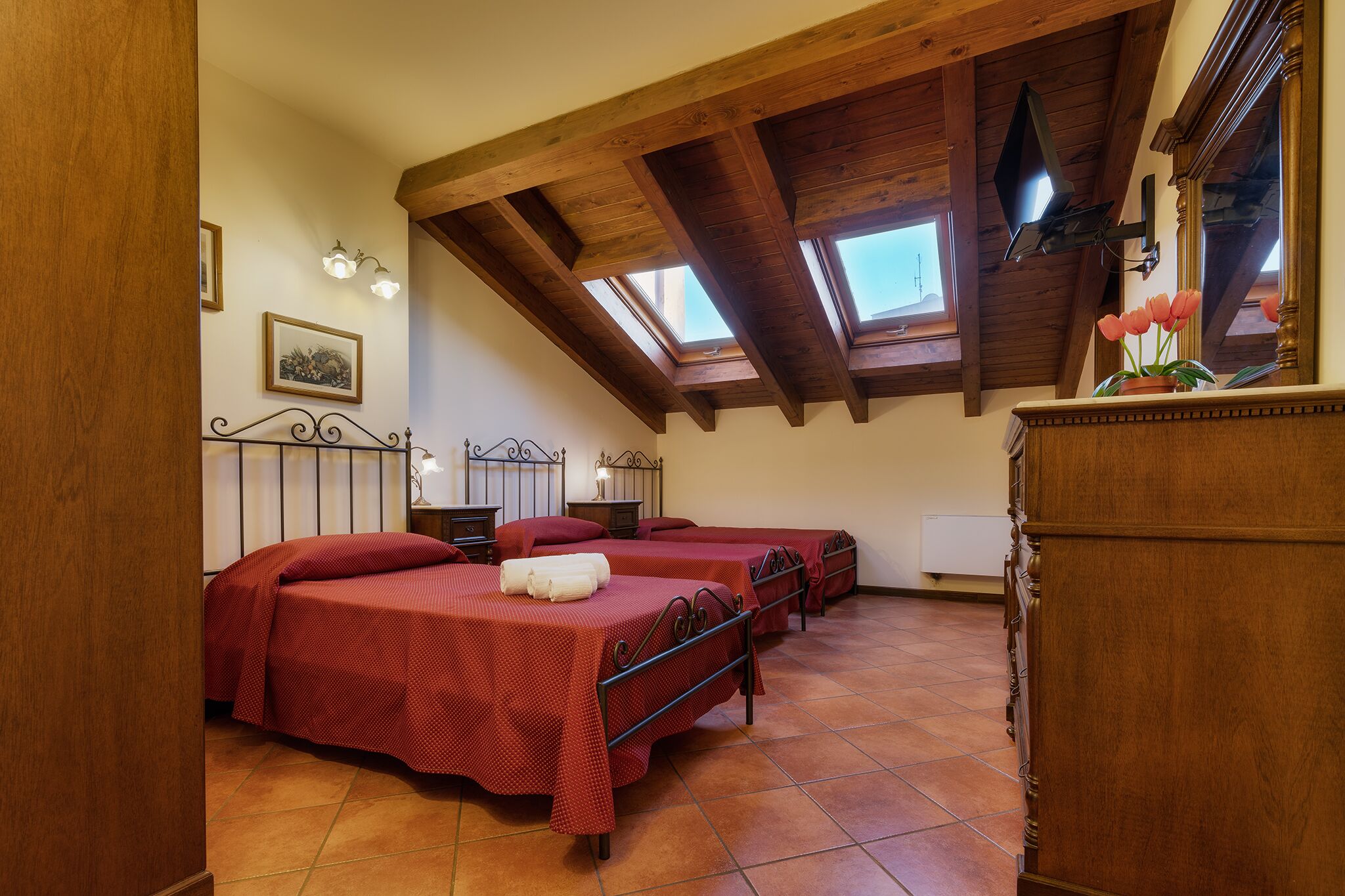 A room with three beds, wooden beams, a skylight, and a mirror.