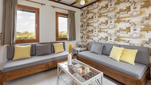 A living room with two grey sofas, yellow patterned cushions, a coffee table with a vase and candles, and a patterned wall. - Trikorfo Beach (Polygyros)