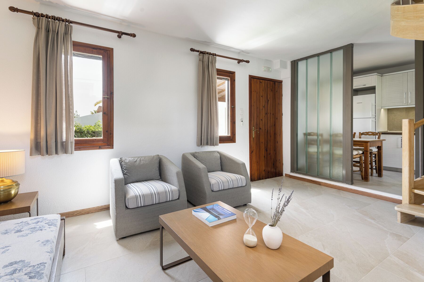 A modern living room with two grey armchairs, a wooden coffee table, and a book.