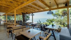 An outdoor dining area with wooden tables and chairs, a sofa, and hanging lanterns. - Trikorfo Beach (Polygyros)
