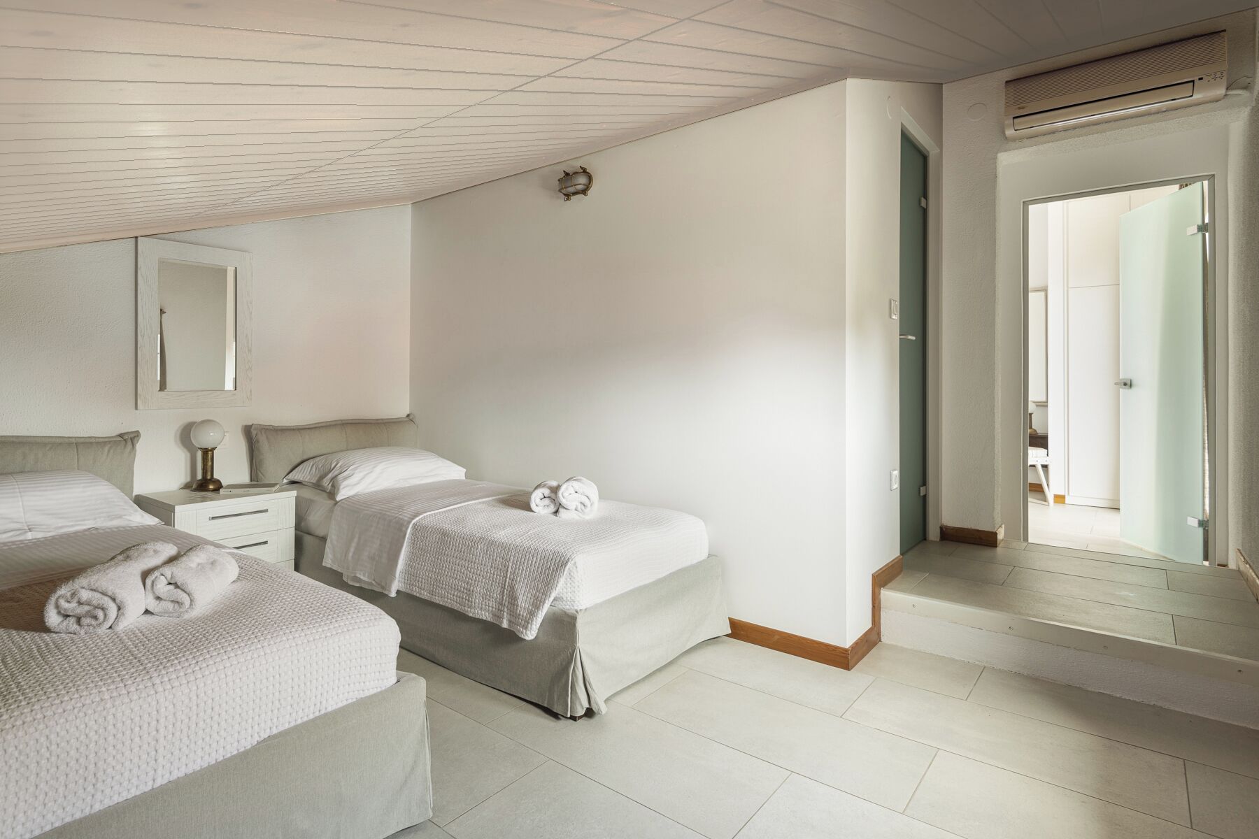 Quarto de hotel com duas camas, uma mesa de cabeceira, um espelho e um aparelho de ar condicionado.