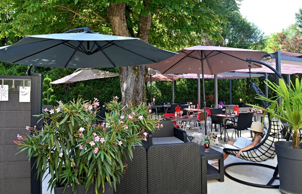 An outdoor patio area with wicker furniture, umbrellas, and a dining setup.