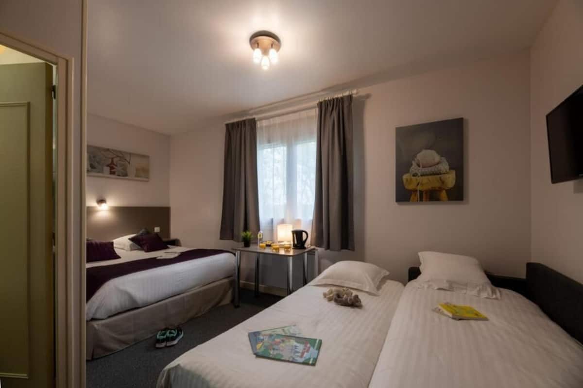 A hotel room with two beds, a desk with a lamp, a window with curtains, and a painting on the wall.