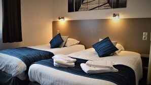 A hotel room with two beds, each with a blue headboard, white bedding, and a folded towel on the bed. - Hôtel Le Prieuré (Saint-Marcel)