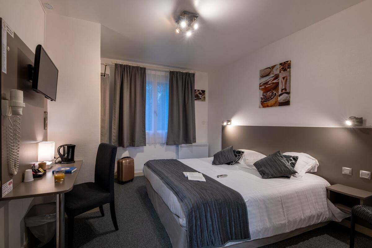 A hotel room with a bed, desk, chair, and a window with curtains.