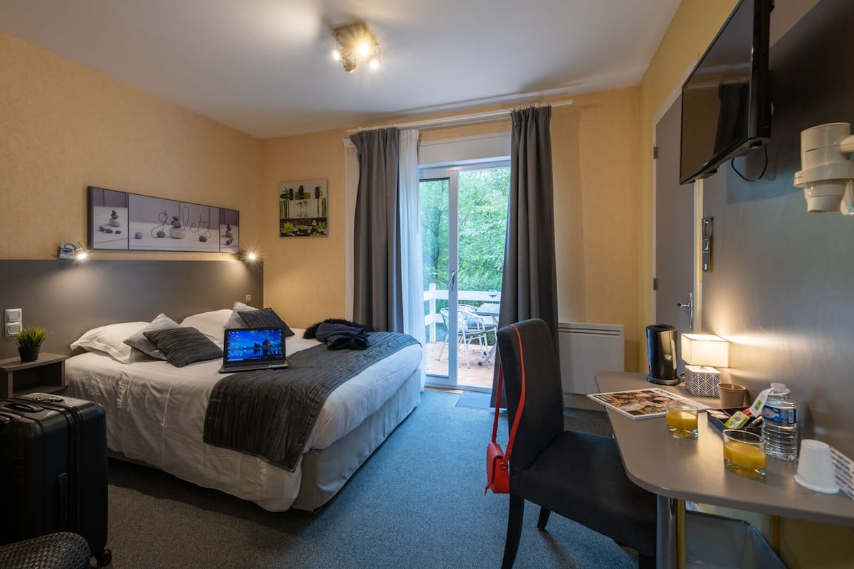A hotel room with a bed, a desk with a chair, a TV, and a window with curtains.