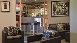 A bar area with wicker furniture, a bartender, and a clock on the wall. - Hôtel Le Prieuré (Saint-Marcel)