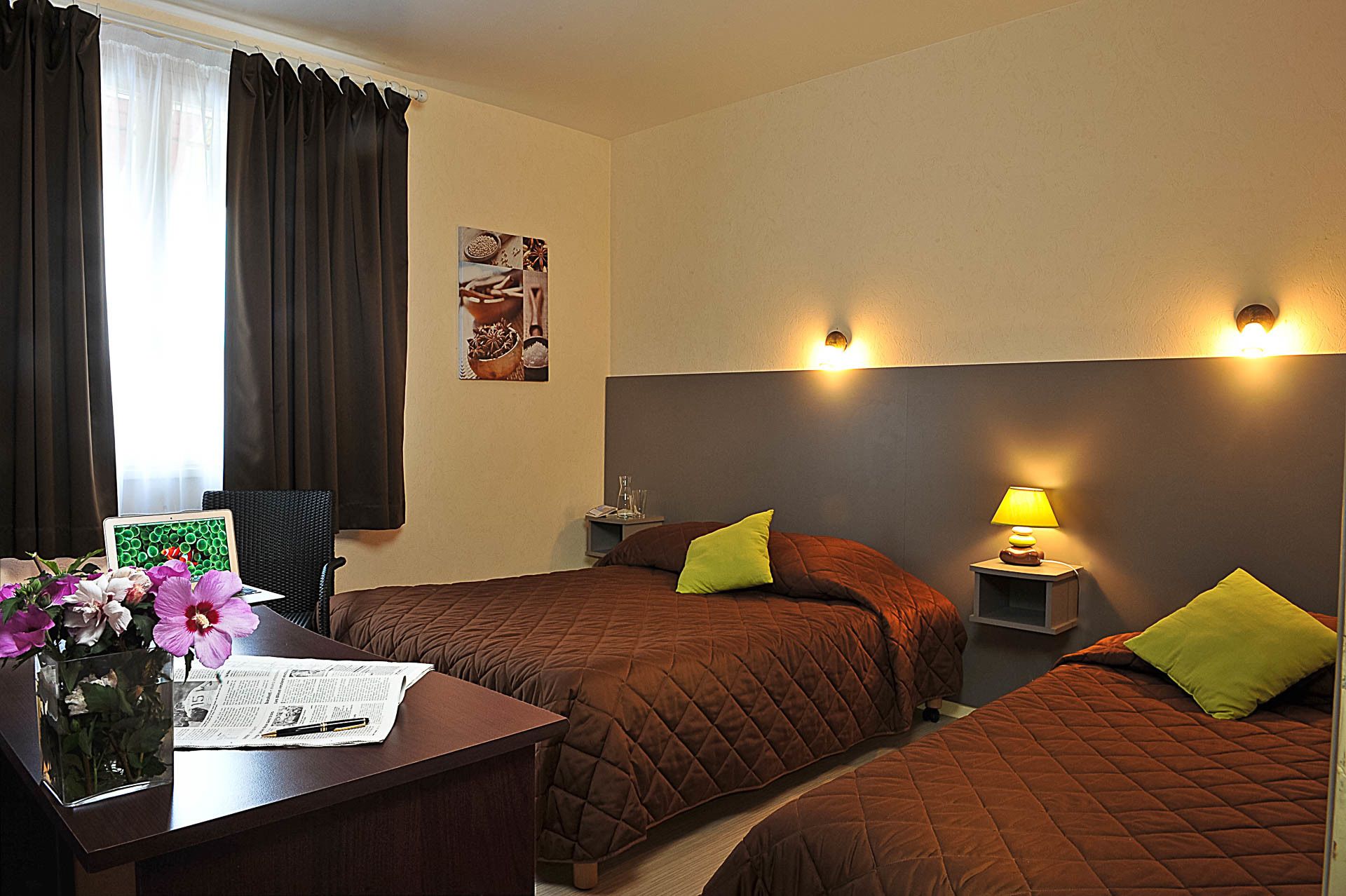 Hotelkamer met twee bedden, een bureau met een laptop, een bloemenvaas en een aan de muur hangend schilderij.