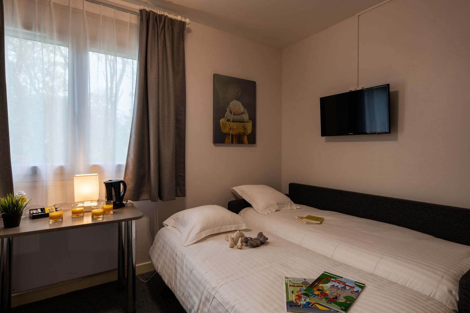 Ett hotellrum med en säng, ett nattduksbord med en lampa, en tv och ett fönster med gardiner.