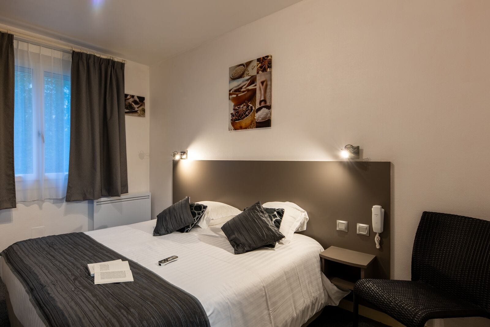 Una camera d'albergo con un letto grande, un comodino con una lampada, una sedia e un telefono fissato alla parete.
