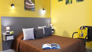 A hotel room with a brown quilted bedspread, two bedside lamps, a nightstand with a lamp and books, and a wall with framed pictures.