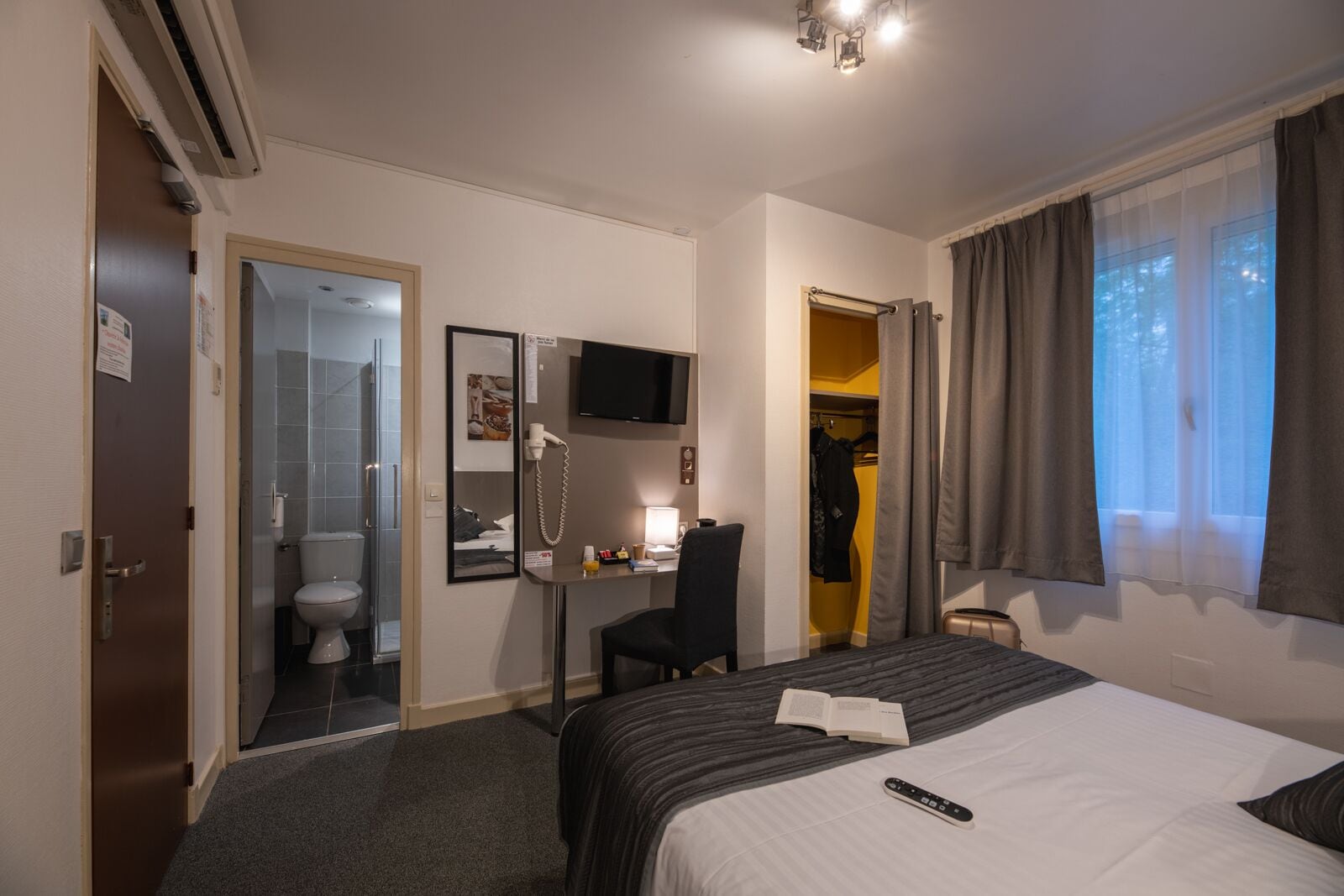 Une chambre d’hôtel équipée d’un lit, d’un bureau, d’une chaise, d’une télévision, d’une douche et d’une armoire.