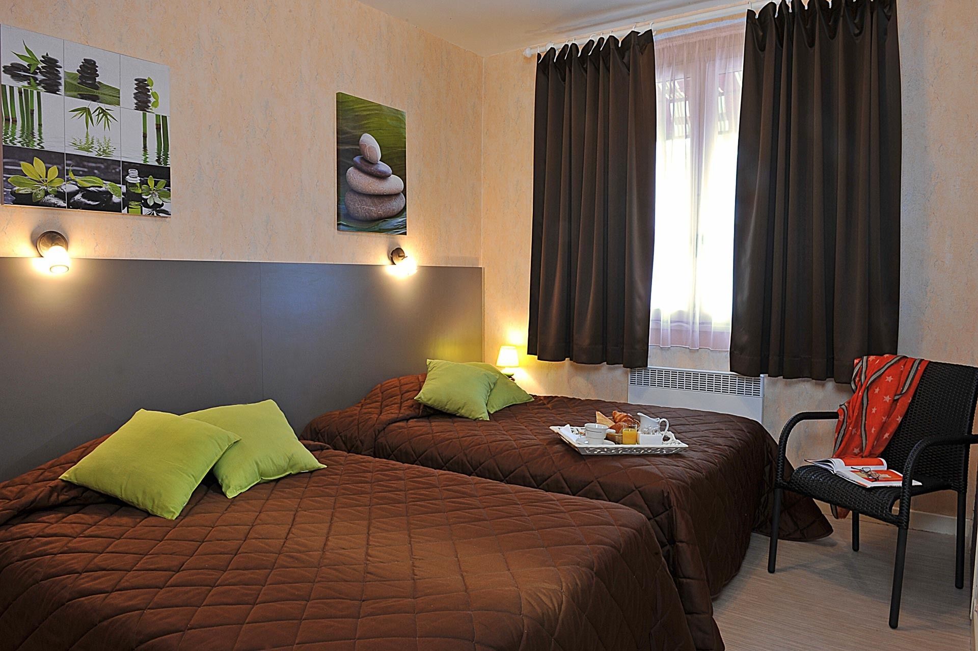 A hotel room with two beds, a chair, a table with breakfast items, and a wall with a nature-themed artwork.