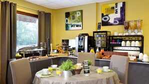 A breakfast area with a buffet, coffee machines, and a wall with art and a 'NEWS' sign. - Hôtel Le Prieuré (Saint-Marcel)