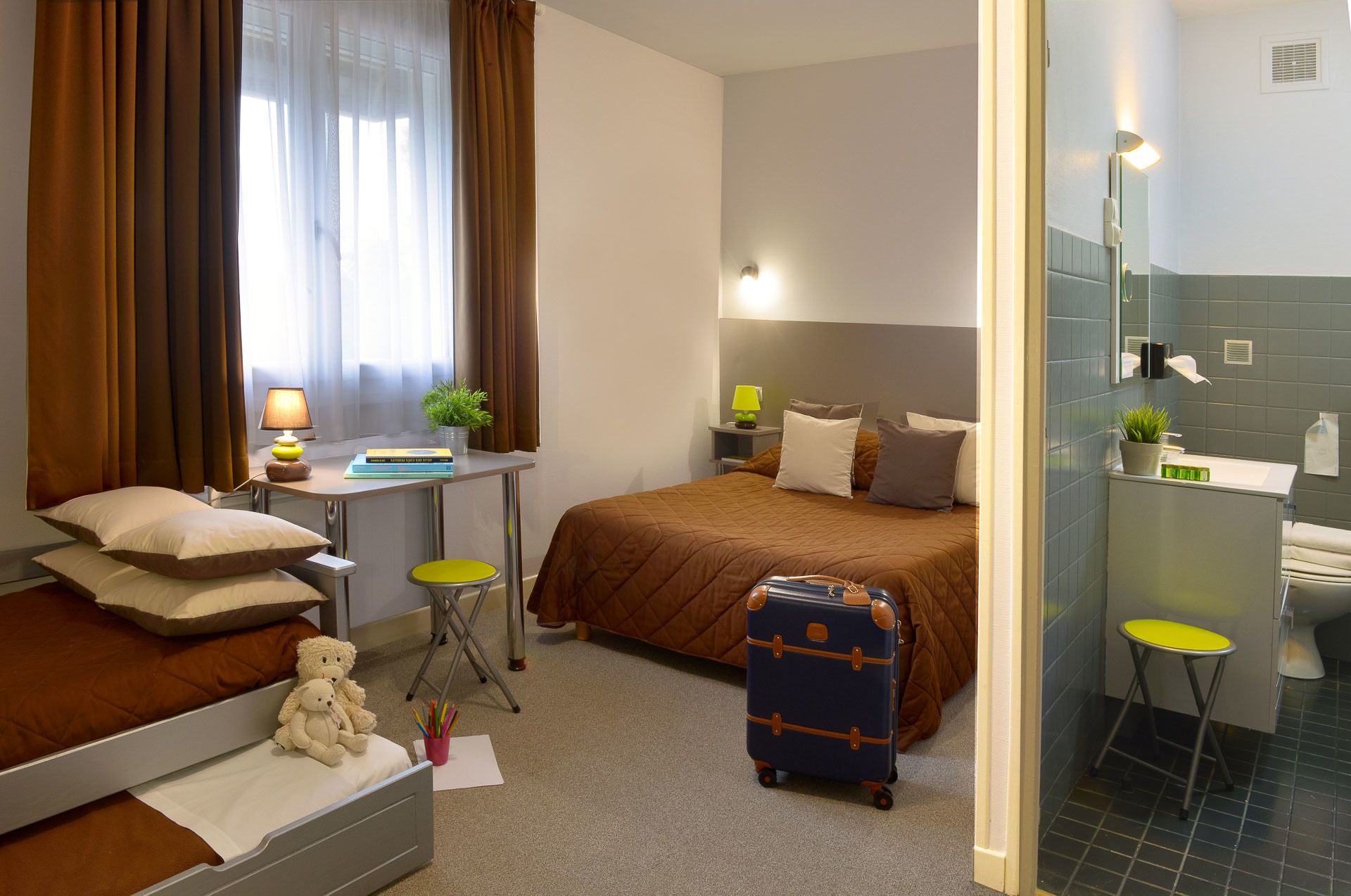 Una habitación de hotel con una cama, mesita de noche, lámpara y una maleta.