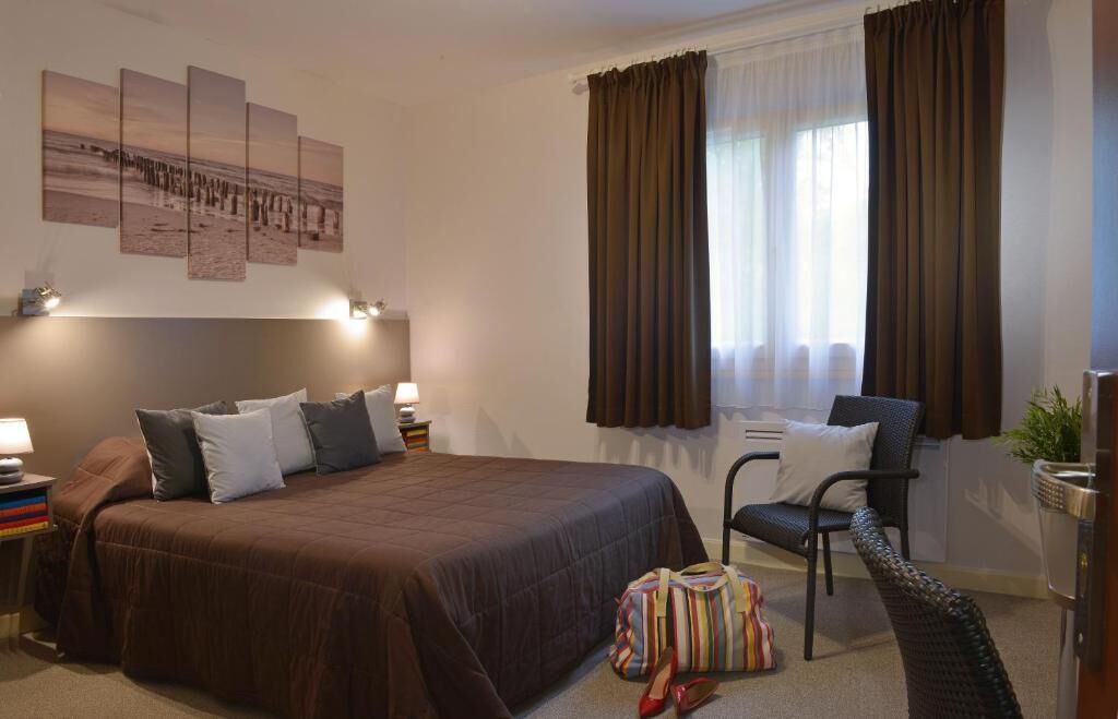 A hotel room with a large bed, a chair, a desk, a lamp, and a window with curtains.
