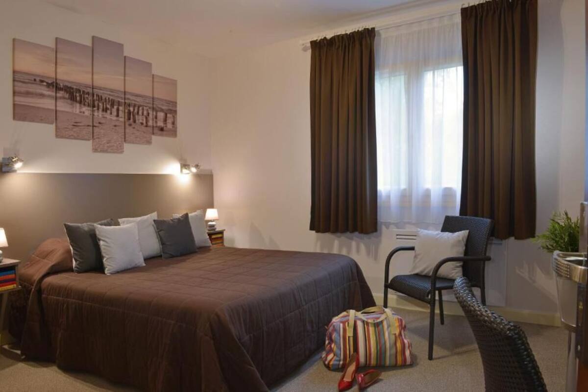 A hotel room with a large bed, a chair, a desk, a lamp, and a window with curtains.