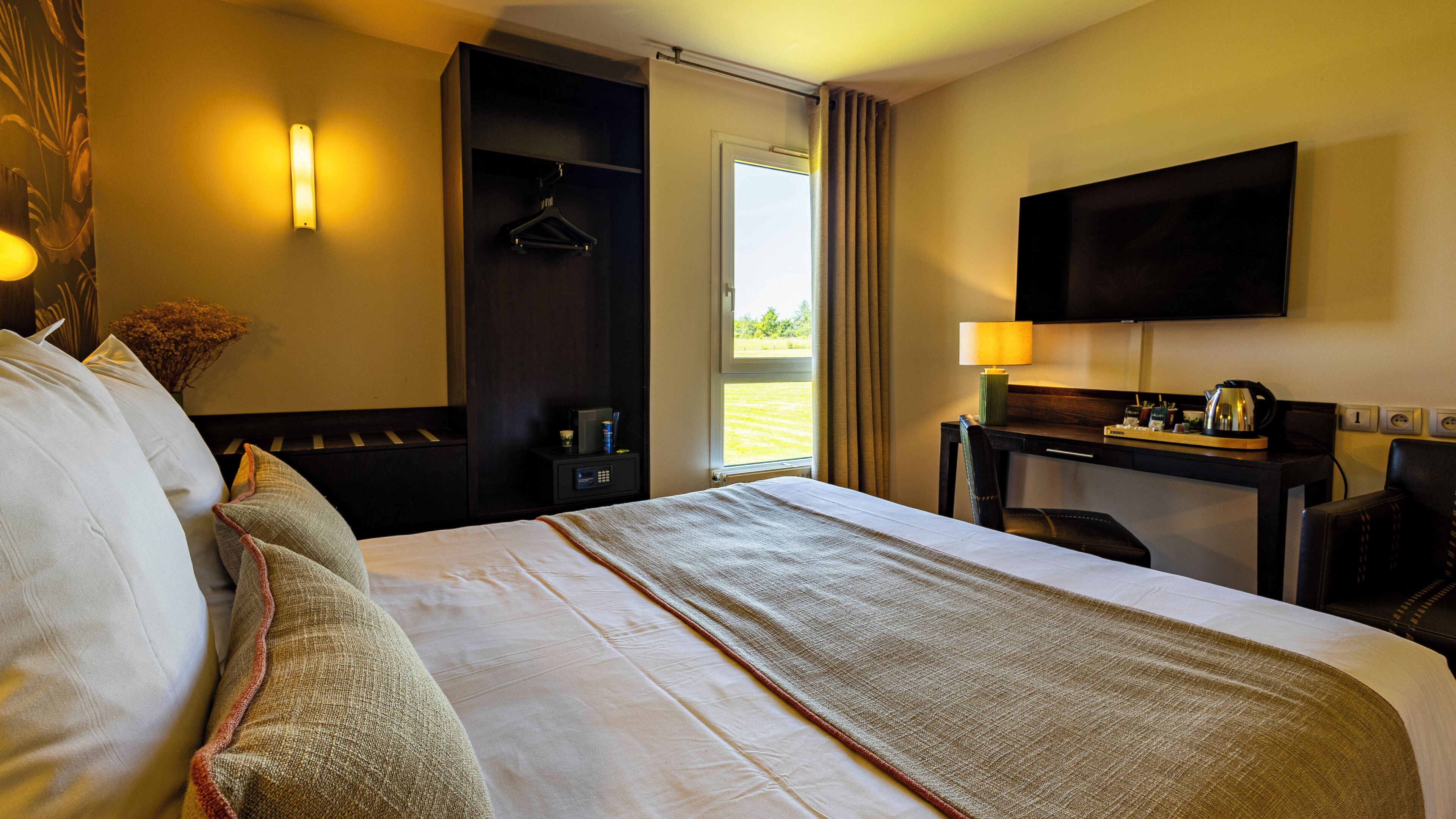 Habitación de hotel con una cama grande, un escritorio con silla, televisor montado en la pared y ventana con cortinas.