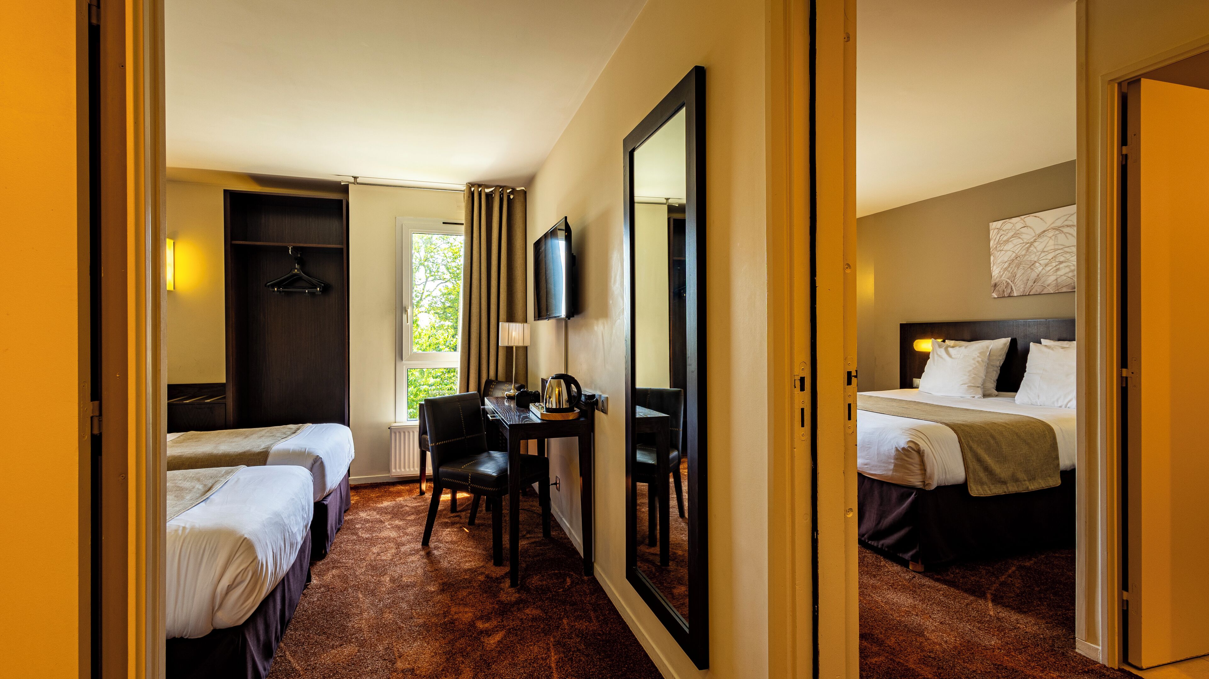 A hotel room with two single beds, a desk with a chair, a television, and a large mirror.