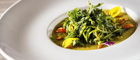 A white bowl of green soup with vegetables and herbs on a wooden table.
