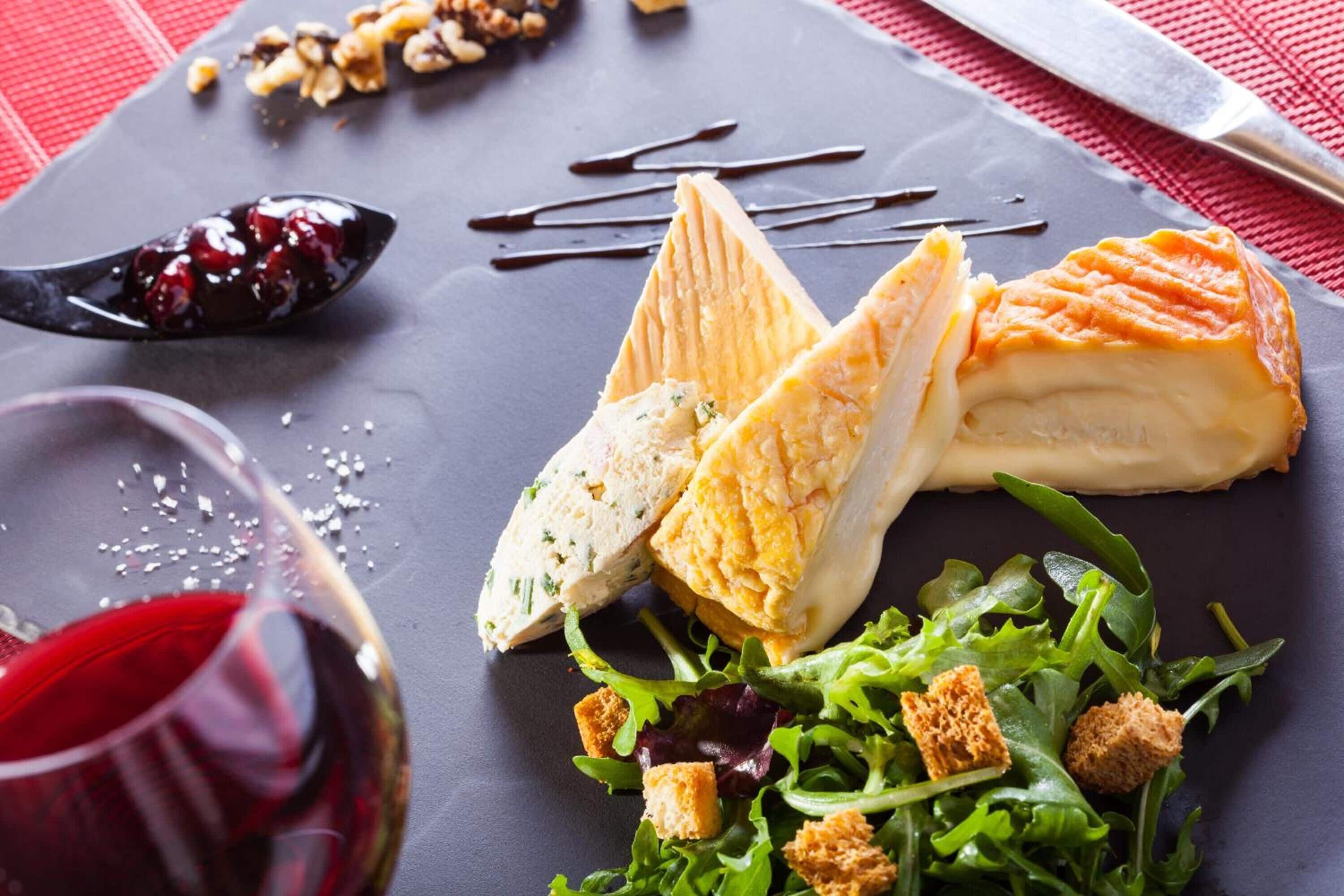 A cheese platter with various cheeses and a salad on a slate board.