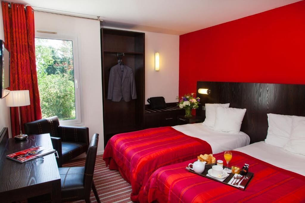 Ein Hotelzimmer mit zwei Betten, einem Schreibtisch, einem Stuhl, einem Kleiderständer und einem Frühstücksbrettchen.
