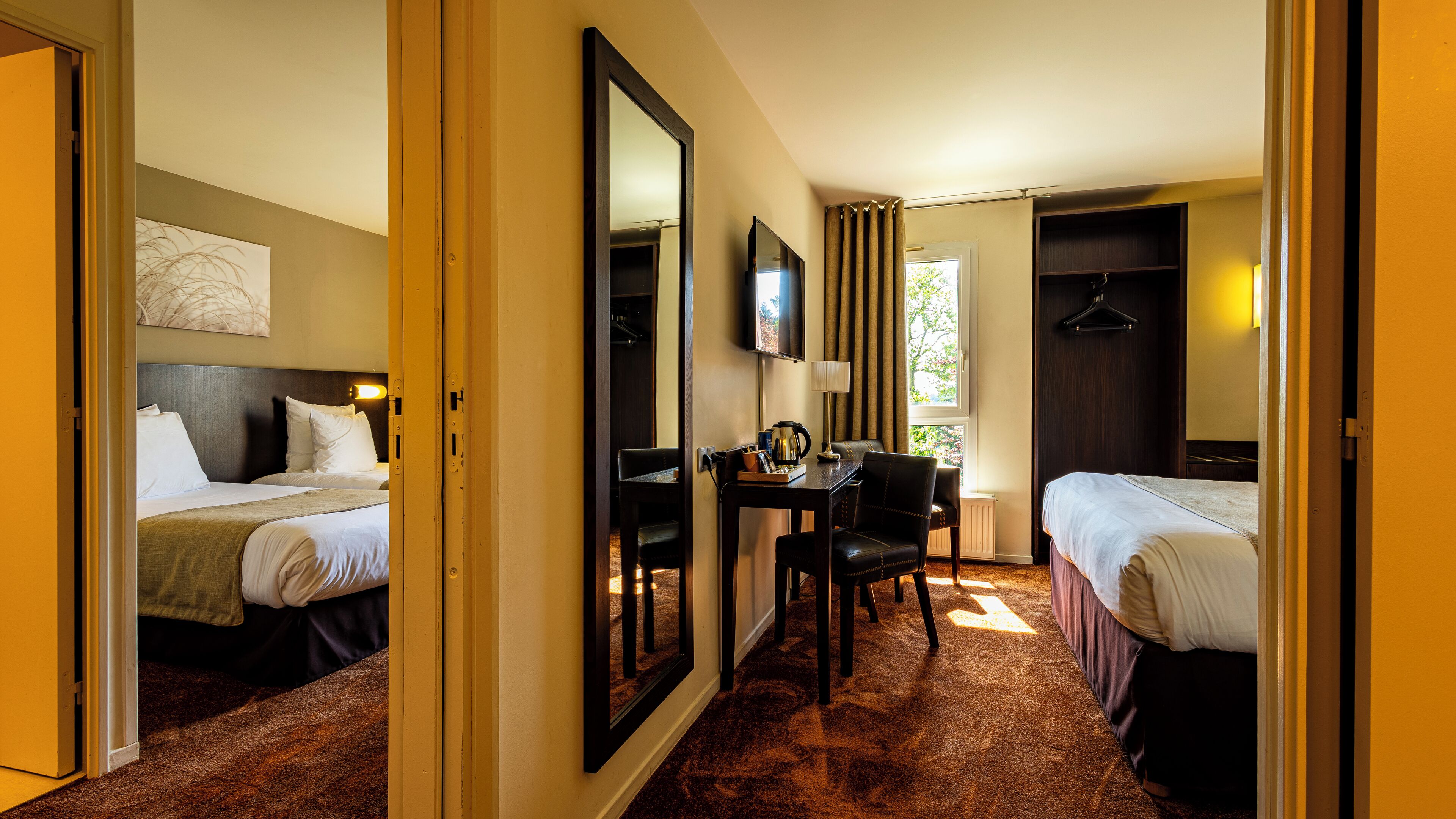 A hotel room with two beds, a desk with a chair, a television, and a large mirror.