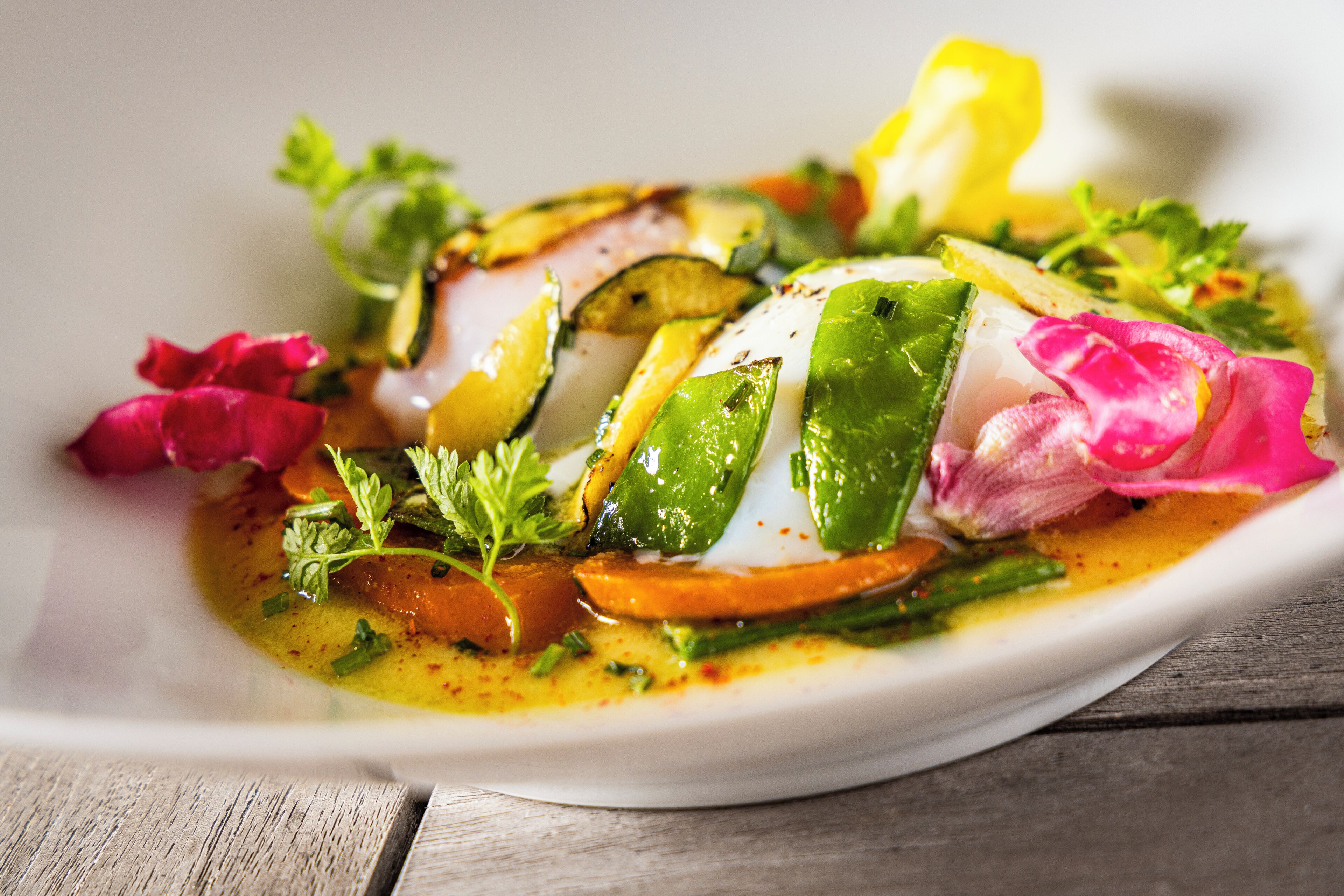 Une assiette blanche contenant un plat composé de poisson en tranches, de légumes et d’herbes aromatiques.