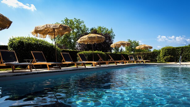 Zona junto a la piscina con sillones de descanso y sombrillas de paja.