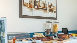 Een ontbijtbuffet met diverse gerechten, een koffieapparaat en een stadsgezichtschilderij aan de muur.