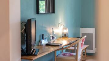 A room with a desk, chair, computer, lamp, and a window with curtains.