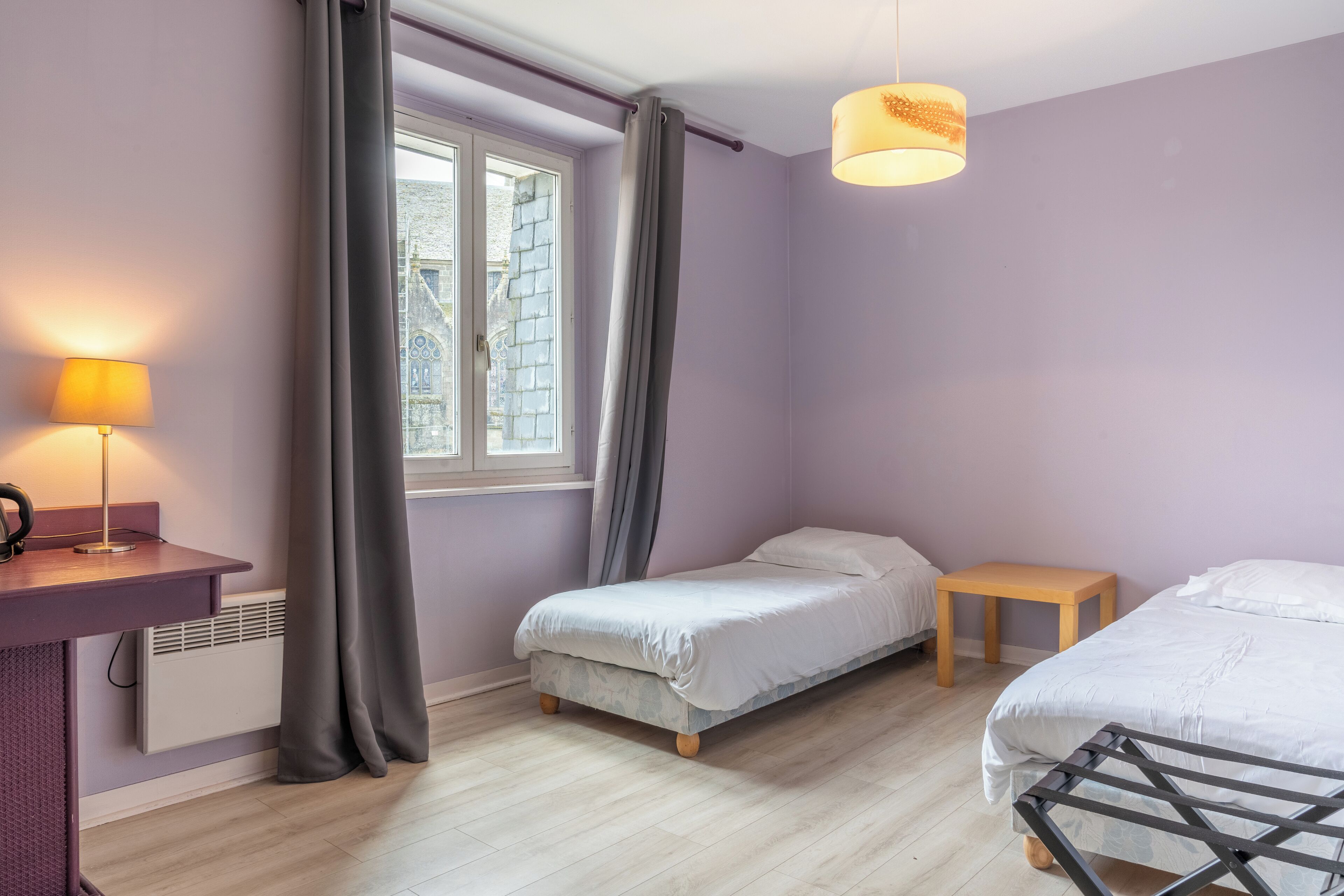 A bedroom with two beds, a window, a lamp, and a small table.