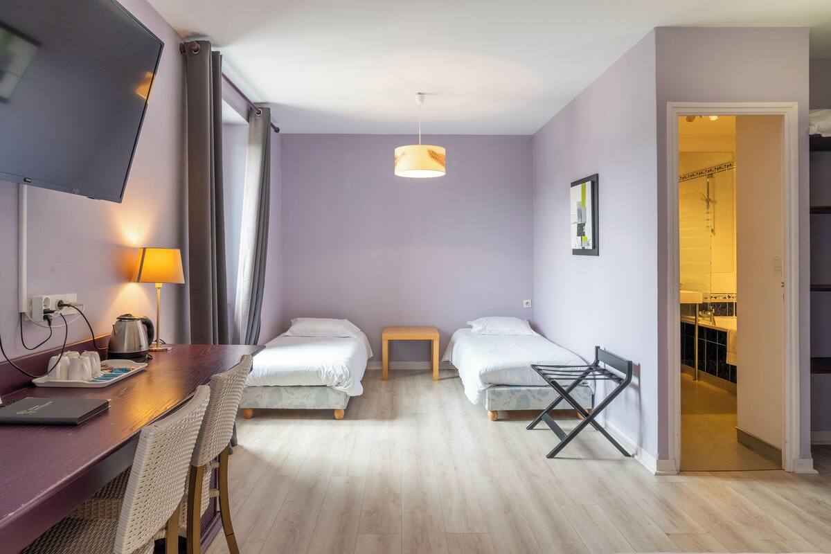 Una habitación de hotel con dos camas, un escritorio con silla, un televisor y una lámpara.