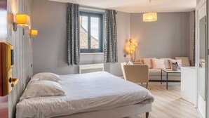Un dormitorio con cama, una silla, un sofá y una ventana con cortinas.